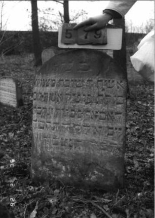Grabstein 579 (Index: 100115320) Material: Sandstein Zustand: verwittert Maße HxBxT: 83x55x10 cm Beschreibung: Stele mit Rundbogenabschluß: Grabstein 579