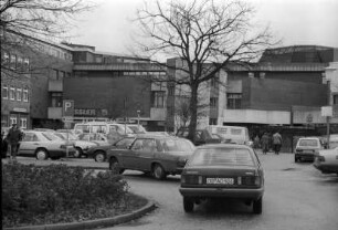 Manfred-Samusch-Straße: Pkws beim Rangieren, dahinter Parkplatz, Autos: hinten Rückfront von Kaufhaus Nessler