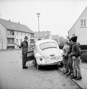 Meisenweg: Panzerfaust im Vorgarten: Mann mit Panzerfaust in Hand vor geöffneter Fahrertür eines VW Käfers: rechts Kinder und Jugendliche: dahinter Wohnhäuser: 26. November 1966