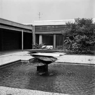 Kunst im öffentlichen Raum: Klosterbergen: Klosterbergenstraße: Volksschule Klosterbergen [später Grundschule]: Brunnen mit Steinskulptur "Quellsteine" von Bildhauer Ulrich Beier: vorn Wasserbecken: dahinter Schulgebäude mit Sträuchern und Bäumen