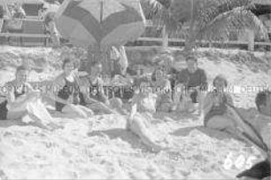 Touristen in Badekleidung mit Drinks am Strand liegend