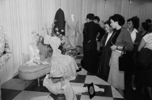 Mehrere Frauen betrachten auf der Leipziger Herbstmesse 1955 am Stand von "Elite Bekleidung" ausgestellte Sommerkleidung