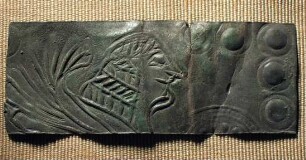 Fragment eines starken Blechs. Als Verzierung dient eine Sphinx, von der nur der Kopf und der Flügel erhalten ist. ...