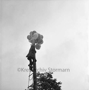 Dorffest: eine Person holt einen Luftballon von einem Mast herunter