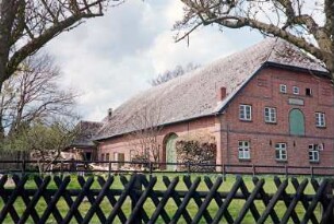 Bundesstraße (20): giebelständiges Bauernhaus aus Backstein: Straßenfront mit Sprossenfenstern, in Obergeschoss Ladeluke: Traufseite mit Scheunentor, an Hauswand Holzstapel, hinten links Querbau mit Tor: vorne Jägerzaun