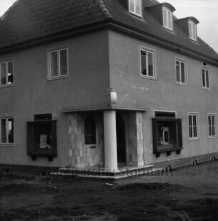 Schmalenbeck: Apotheke in Neubau eines Wohn- und Geschäftshauses: Eingangsbereich an Hausecke mit Apothekenschild und Schaufenstern: vorn unbefestigtes Gelände
