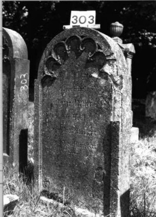 Grabstein 303 (Index: 100085250) Maße HxBxT: 123x66x14 cm Beschreibung: Stele, eingezogener Rundbogenabschluß, Schriftfeld eingetieft mit Maßwerk: Grabstein 303
