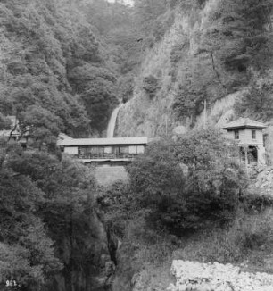 Honshū. Nunobiki-Wasserfall bei Kobe mit überdachter Brücke und Gebäuden beiderseits der Schlucht