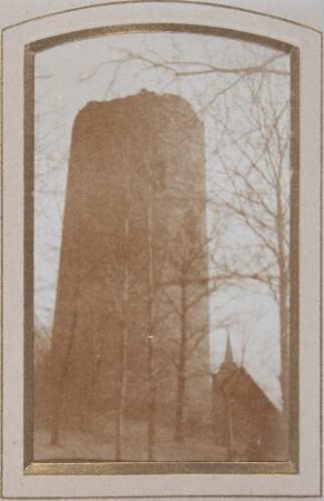 unbekannter Ort: Ruine von Rundturm: davor Bäume: im Hintergrund Gebäude, Kirchturm