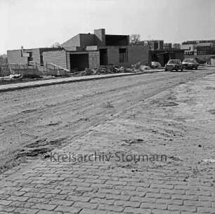Ehmkenberg: Wohnhäuser in unterschiedlichen Baustadien: links Pkws: dahinter Wohnblocks: vorn teilweise unbefestigte Straße: 19. März 1972