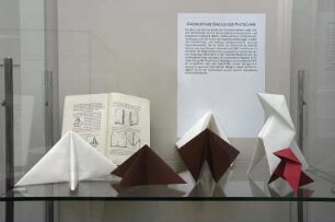 Serviettenfaltkunst. Dresden-Pillnitz, Kunstgewerbemuseum. 2007.06.30-10.31. Standvitrine mit gefalteten Servietten von J. Sallas
