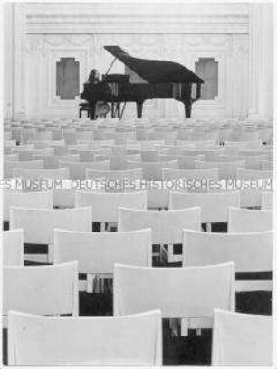Junge Frau spielt in einem leeren Saal Klavier (Altersgruppe bis 14)