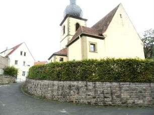 Kirche von Nordwesten (Langhaus im Kern Romanisch mit Veränderungen um 1716-Barocke Überarbeitung) über Kirchhofmauer (Wehrgang mit Steinbrüstung abgetragen)