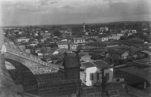 Blick von einer gotischen Kirche auf eine Stadt mit Minarett und Palmen