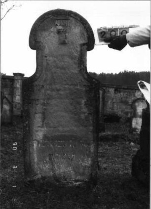 Grabstein 200 (Index: 100115004) Material: Sandstein Zustand: sehr stark verwittert mit sehr starkem Textverlust Maße HxBxT: 146x58x11 cm Beschreibung: Stele mit Hufeisenbogen, verwitterte Darstellung im Giebel: Grabstein 200