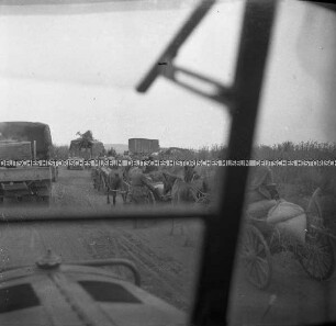 LKW der Wehrmacht und Soldaten auf Pferdewagen auf einer Landstraße, aus einem LKW heraus fotografiert