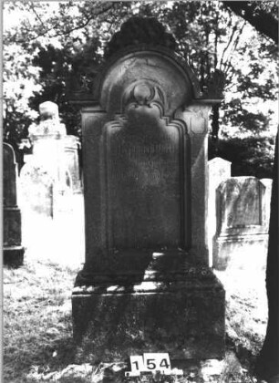Grabstein 154 (Index: 100085441) Maße HxBxT: 151x67x24 cm Beschreibung: Stele, profil. Sockel, eingezog. Rundbogenabschl. m. Akroteren, Schriftfeld eingetieft: Grabstein 154