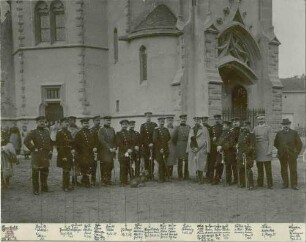 Generalstabsreise 1897, zwanzig Personen (Offiziere und ein Zivilist) in Uniform und Mütze vor einem Kirchenbauwerk stehend, im Hintergrund Zuschauerinnen, Bilder vorwiegend in Halbprofil