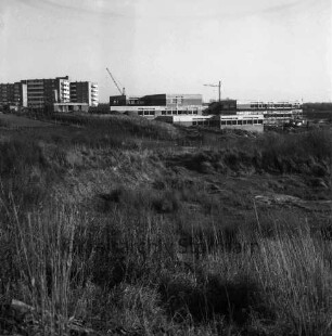 Schule am Masurenweg [Dörfergemeinschaftsschule, Grund- und Hauptschule]: Rohbau: links Wohnblocks: dahinter Baukräne: vorn Wiese, Zäune, Garten, Erdhaufen: 11.11.1972