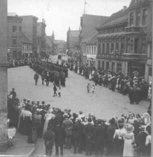 Straßenbild mit zwei Militärs und einem Zivilisten beim Abschreiten einer Ehrenformation