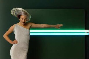 Neonhut, Aufnahme für „Event“ : Model mit Neonhut und Lurex-Kleid vor Neonröhren