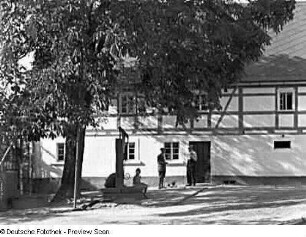 Bischofswerda-Schönbrunn. Gehöft (19. Jahrhundert). Wohnhaus. Hofansicht (Teilansicht) mit Dorfbewohnern an einer Handschwengelpumpe vor dem Wohnhaus