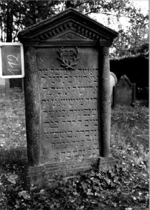 Grabstein 112 (Index: 100111232) Material: Sandstein Zustand: gut Maße HxBxT: 145x74x20 cm Beschreibung: ädikulaartige Stele mit Halbsäulen, getreppter Sockel, giebelartiger Abschluß mit Verdachung Symbolik: gekreuzte Zweige, Blüte, Zackenfries: Grabstein 112