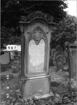 Grabstein 662 (Index: 100099725) Maße HxBxT: 213x60x25 cm Symbolik: Blumenkranz Besonderheit: kulturhistorisch wertvoll / hist.-wiss. Gründe (Gemeindestellung): Grabstein 662