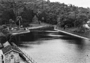 Künstliches Becken : Ein künstliches angelegtes Wasserbecken mit einer Betonumrandung. Im Hintergrund Wald an einem Hang.