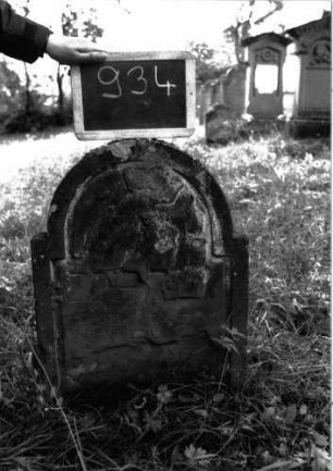 Grabstein 934 (Index: 100103823) Material: Sandstein Zustand: völlig verwittert Maße HxBxT: 69x48x8 cm Beschreibung: Stele, eingezogener Rundbogenabschluss, Schriftfeld durch umlaufende Rille abgeteilt: Grabstein 934
