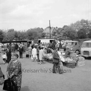 Wochenmarkt: Marktplatz [später Rathausplatz]: Marktstände, Verkäufer, Kunden: Kleintransporter: hinten parkende Autos, Strommast, Wohnhaus, Obstgärten