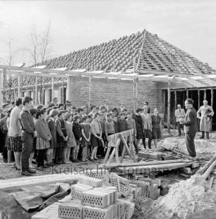 Volksschule Tannenweg: zweiter Erweiterungsbau mit zwei Pavillons: Richtfest: Ansprache von Bürgermeister Herbert Rübner: links und dahinter Schüler, Lehrer und Gäste: hinten eingedeckter Pavillon: vorn Sandhaufen und Baumaterial