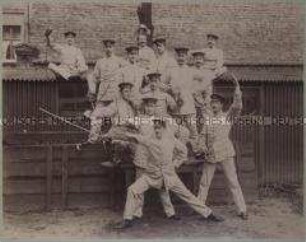 Königliche Militär-Turnanstalt zu Berlin, Winterkurs 1894/1895 - lustiges Gruppenbild von Offiziersschüler mit Degen, einer mit Narrenkappe