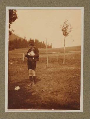 Raimund von Hofmannsthal mit einem Kaninchen auf einer Wiese in Aussee, stehend