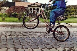Jugendlicher Radfahrer zeigt einen Wheely, Hauptstraße Marienborn, 1993. Im Hintergrund die Orangerie