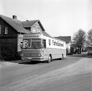 Bücherbus am Straßenrand vor Wohnhaus: im Hinterfgrund Straßenbäume, parkender Pkw