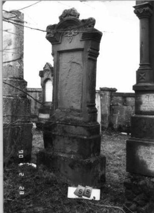 Grabstein 55 (Index: 100114897) Material: Sandstein Zustand: leicht verwittert, Texttafel fehlt Maße HxBxT: 214x66x27 cm Beschreibung: Stele auf gestuftem Sockel, überstehender und gestufter, eingezogener Rundbogen mit Akroterie und Voluten, Blatt im Giebel, vertiefter Textteil, eingesetzte Texttafel: Grabstein 55