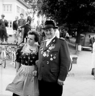 Ahrensburger Schützengilde: Schützenfest und Kreisverbandsfest: Stormarnplatz: Schützengilde-Kommandeur Walter Hauschildt mit Ehefrau Elfriede Hauschildt: hinten abgestellte Fahrräder, Mauer, Personen, Kleintransporter, Bäume: links im Hintergrund Bruno-Bröker-Heim