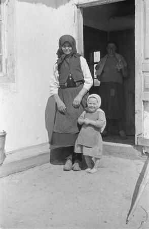 Zweiter Weltkrieg. Zur Einquartierung. Sowjetunion. Kleines Mädchen mit Großmutter vor dem Eingang einer Bauernhütte. Im Haus die Kindesmutter