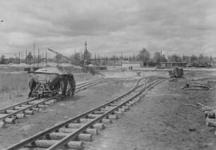 Industrie-Kraftwerk. Baustelle mit Feldbahn und Förderband, im Vordergrund schieben mehrere Frauen und Männer eine Muldenkipplore : Lauta (Niederlausitz). Industrie-Kraftwerk. Baustelle mit Feldbahn und Förderband, im Vordergrund schieben mehrere Frauen und Männer eine Muldenkipplore