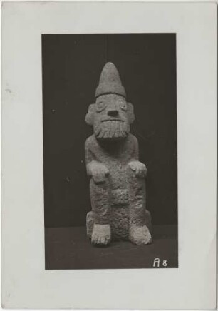 Hockende Tlaloc-Figur aus hellgrauem Kalkstein mit der charakteristischen spitzen Mütze des Frühlingsgottes Xipe ("Fruchtbarkeit als Folge des Regens). Höhe: 37 cm." (B.T)