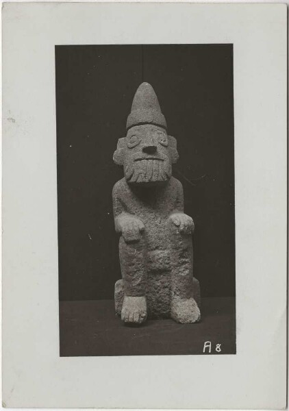 Hockende Tlaloc-Figur aus hellgrauem Kalkstein mit der charakteristischen spitzen Mütze des Frühlingsgottes Xipe ("Fruchtbarkeit als Folge des Regens). Höhe: 37 cm." (B.T)