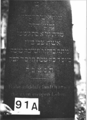 Grabstein 91 (Index: 99898863) Material: Sandstein Zustand: leicht verwittert, Sockel stark verwittert Maße HxBxT: 136x48x24 cm Beschreibung: aufgesockelte Stele mit eingezogenem Rundbogenabschluss, unterer Sockel felsartig gearbeitet: Grabstein 91A
