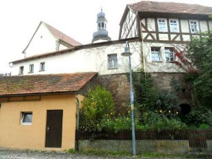 Evangelische Kirche-Ansicht von Westsüdwesten mit Kirche (im Kern Romanisch) über Kirchhofmauer (Wehrgang im 19 Jh abgetragen und Pfarrhaus auf Kirchhofmauer aufgebaut)