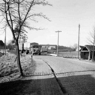 Bundesstraße B 75: alte Straßenführung: Kopfsteinpflaster: rechts kleines Gebäude ohne Gieblewand: dahinter Strommasten: links Baum: dahinter Lkw mit Anhänger und Brücke über die Norderbeste: im Hintergrund Gehöfte und Bäume