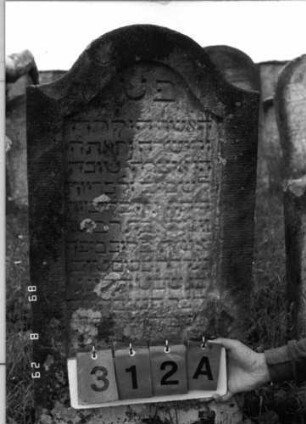 Grabstein 312 (Index: 100107726) Material: grauer Sandstein Zustand: sehr stark verwittert, teilweiser Textverlust Maße HxBxT: 107x50x11 cm Beschreibung: Stele, geschwungener Bogenabschluß, Schriftfeld eingetieft: Grabstein 312A