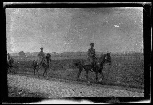 Nicht identifizierbare Ortschaft in Nordfrankreich oder Belgien: 2 Offiziere zu Pferd auf einer schmalen, gepflasterten Landstraße (Distanzaufnahme)