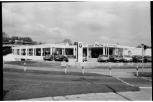 BMW-Niederlassung Adolf Werner: Ostring, Ecke Beimoorweg: Neueröffnung Anbau: Außenansicht: Ausstellungsraum Erdgeschoss, links darunter Tiefebene: rechts Altbau mit Firmenname: davor Außenfläche, Autor, Stele mit Firmenlogo