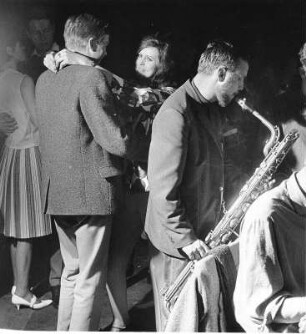 In einer Diskothek. Eine Saxophonspieler unterhält die Gäste. Im Hintergrund wird getanzt.