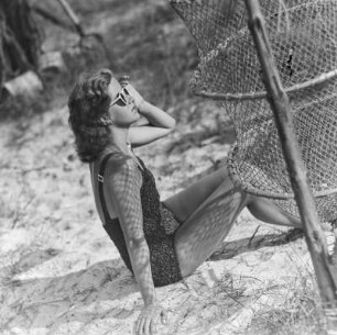 Frau im Bikini mit Sonnenbrille neben einer Reuse am Strand